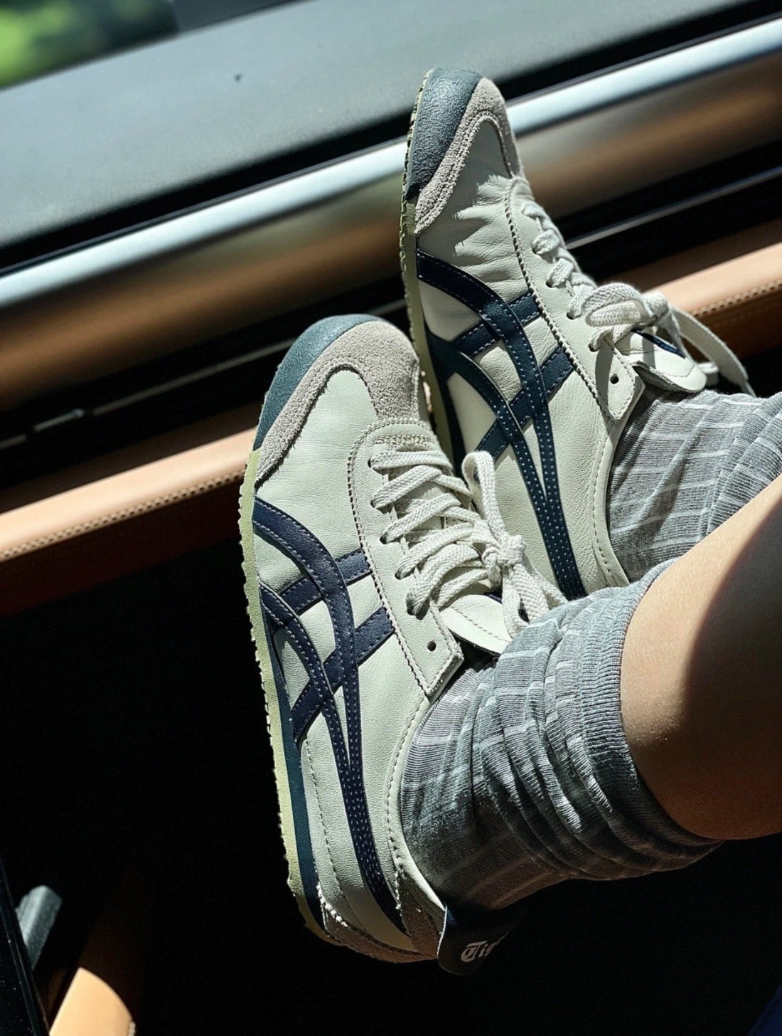 Person wearing light gray sneakers with dark blue accents, sitting inside a vehicle.